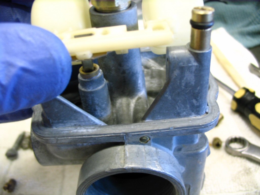 Insert the float needle into the carburetor body and position the float between the hinges.