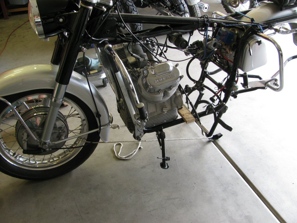 Front engine mounting bolt in place. Center stand prevented from retracting by a length of rope tied around the front wheel.